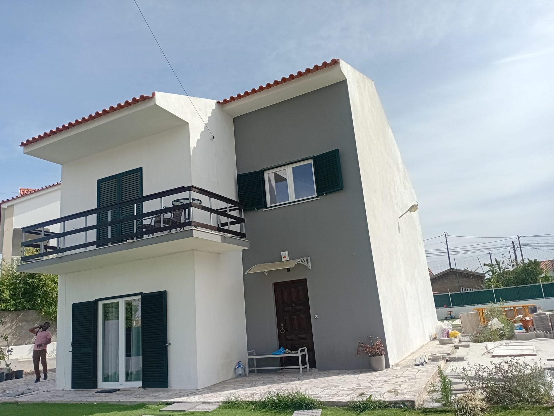 Finished two-storey house with a white and grey façade, a balcony and green shutters