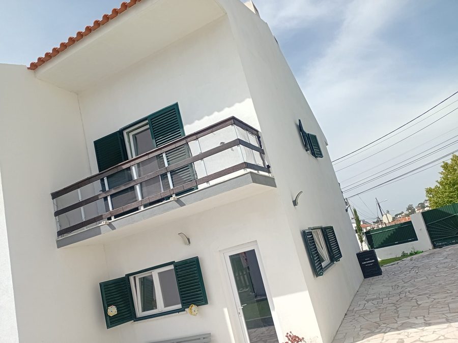 The house's balcony with a metal railing and green shutters