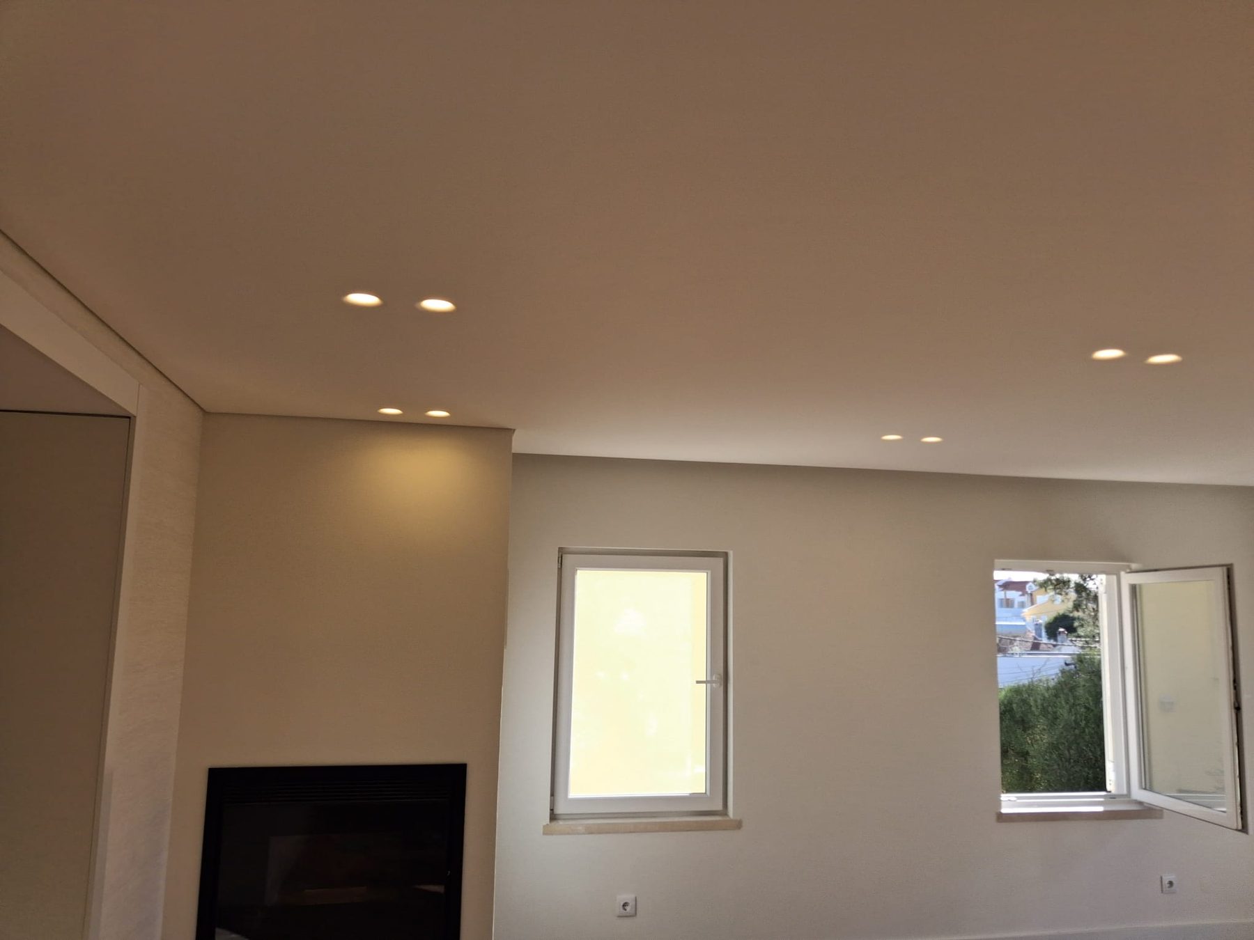 A mesma sala acabada, com a lareira, as paredes pintadas e focos de luz no teto