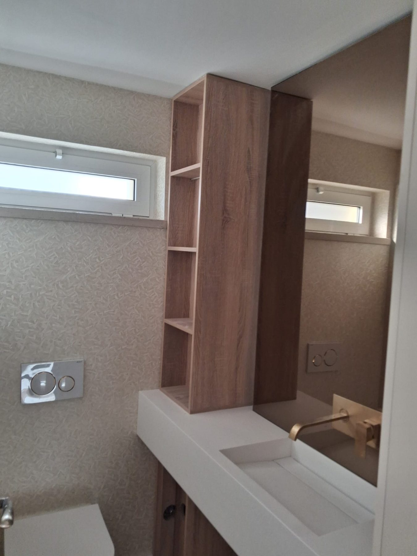 The same bathroom finished, with a white vanity top, a wooden shelving column and a high window