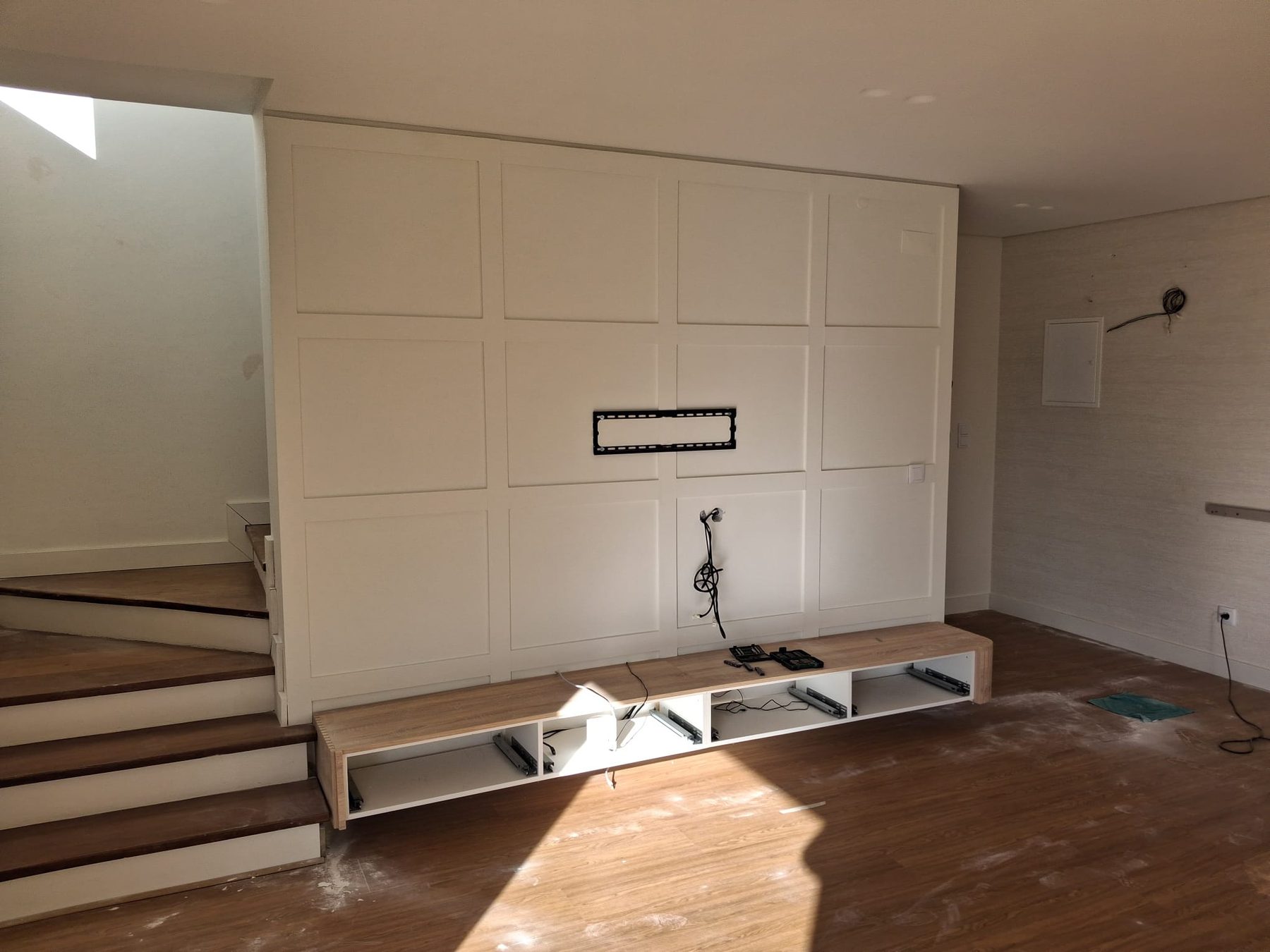 TV wall with white panelling, a low cabinet and the wooden staircase alongside