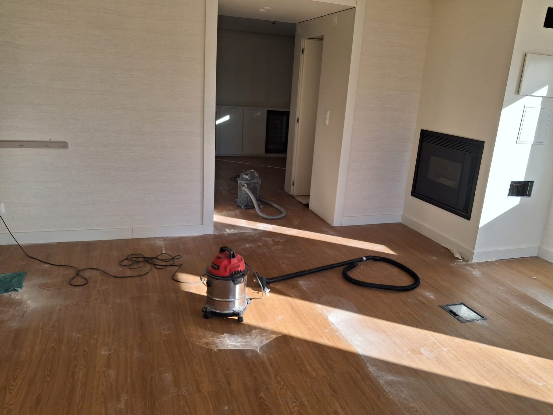 Living room during the works, with dust on the floor, a vacuum cleaner and the fireplace in the background