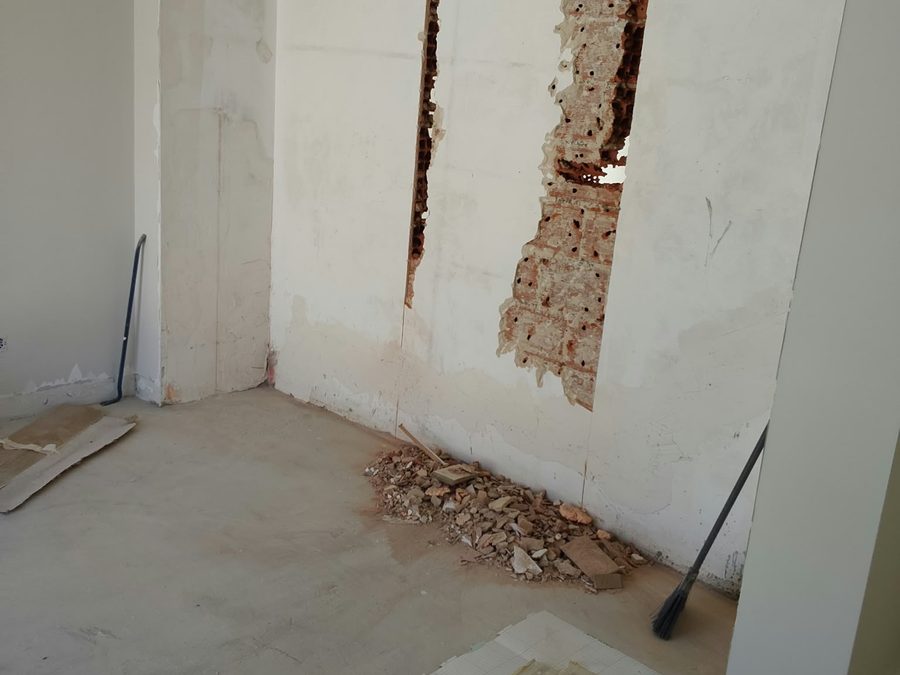Wall broken back to the brick, with rubble on the concrete floor