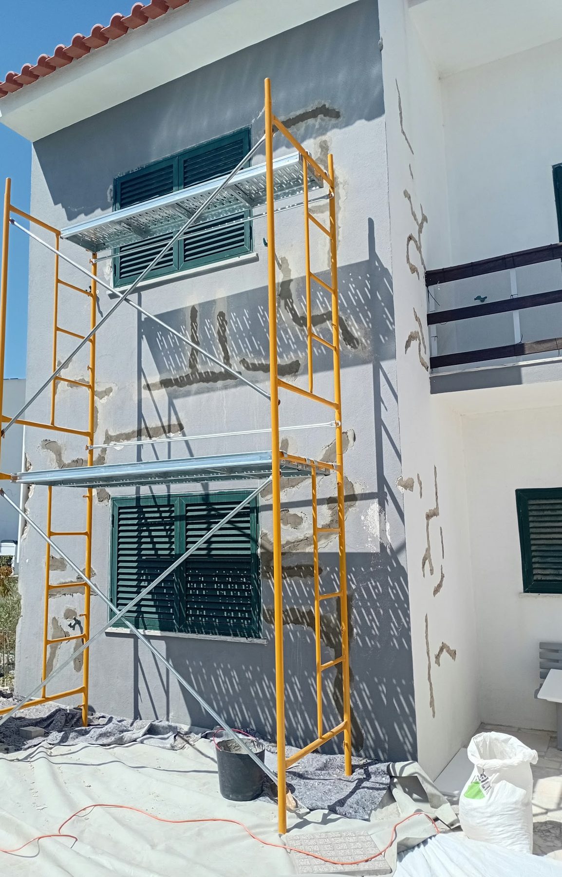 The house façade before the works, painted grey, with cracks opened up and filled and scaffolding in place
